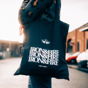 Iron & Fire's black tote bag, being worn over someone's shoulder.
