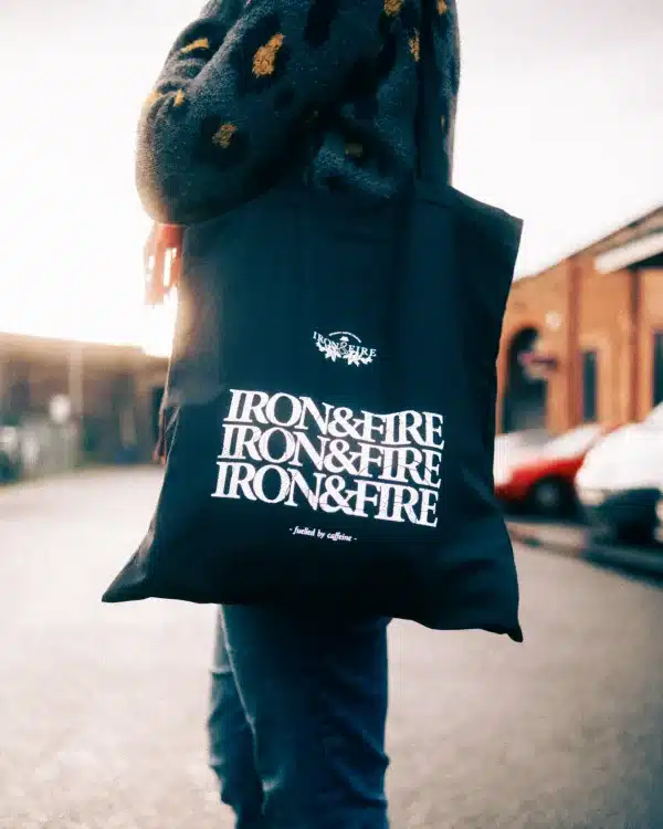 Iron & Fire's black tote bag, being worn over someone's shoulder.