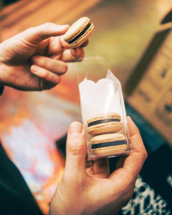 A hand holding a coffee-flavoured macaron that has been removed from the box, where the other two macarons remain.