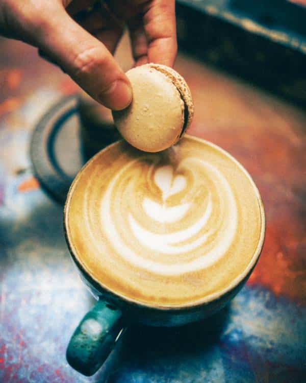A coffee-flavoured macaron being dipped into a latte made from Iron & Fire's Mama New Guinea blend