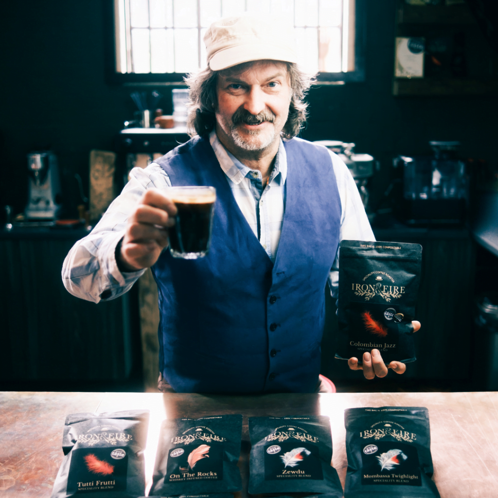 Iron & Fire founder Kev Burrows, lifting a cup of coffee and holding one of Iron Fire's award-winning coffees