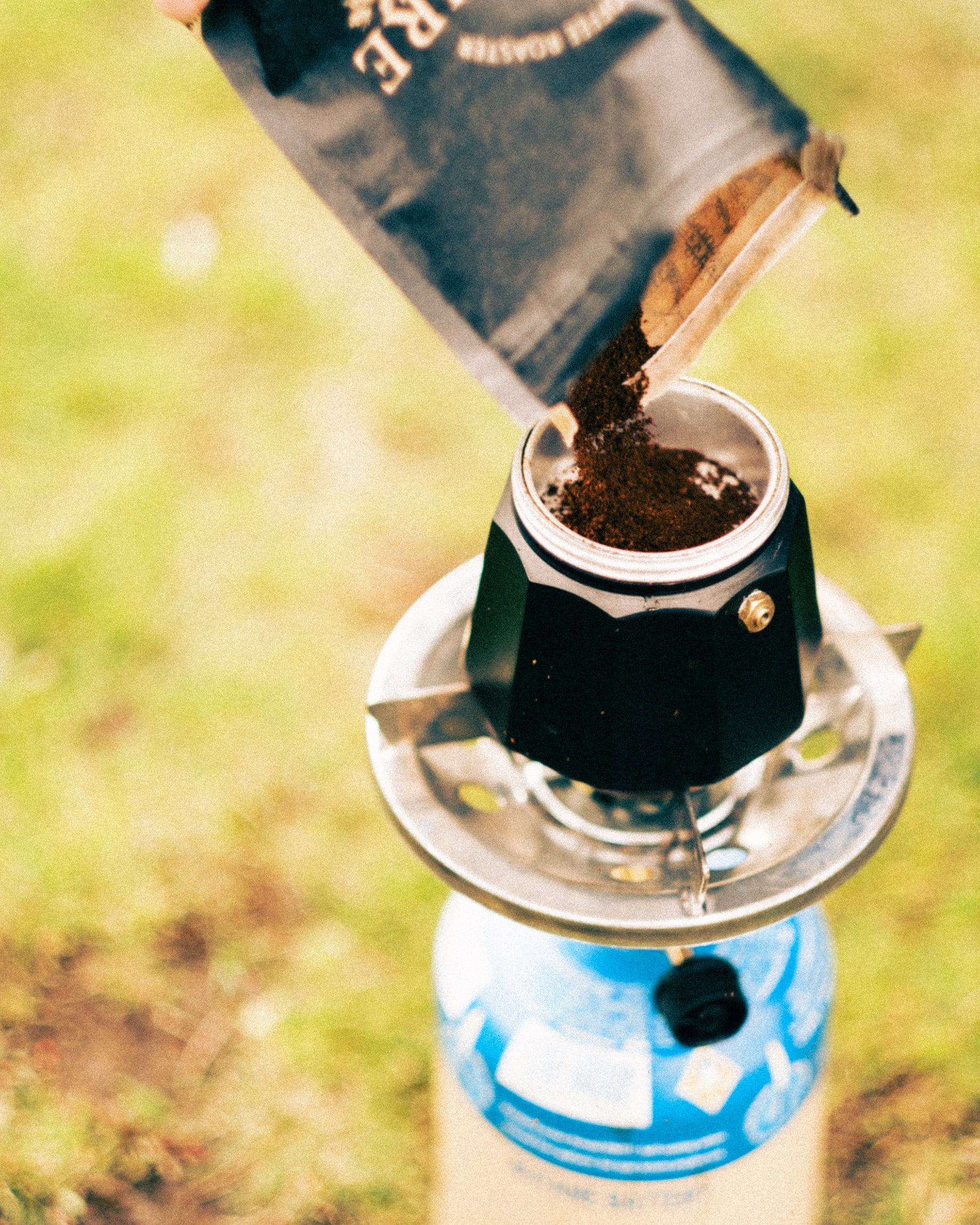 Iron & Fire coffee being poured into the base of a Moka pot on a gas stove outdoors